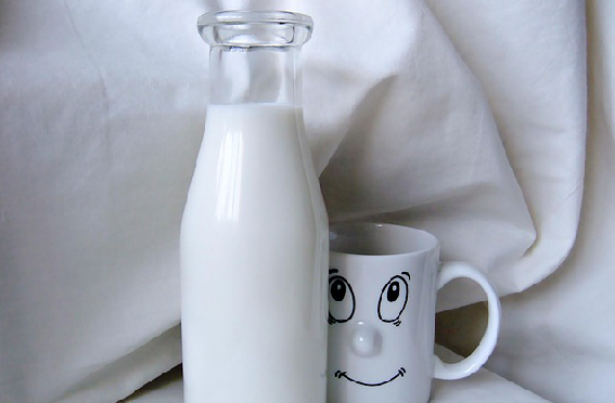 Milch in einer Glasflasche neben einer Tasse mit Gesicht